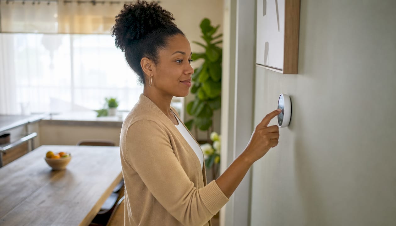 Woman adjusting modern thermostat in home