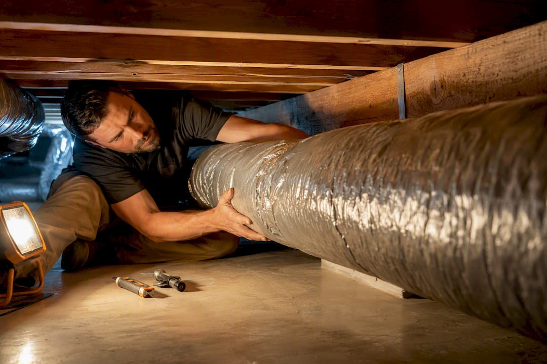 Installer guiding ductwork through a tight crawlspace