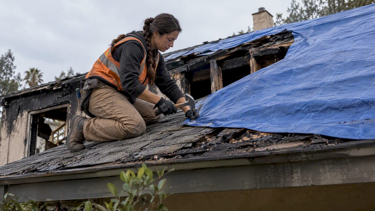Contractor securing tarp over damaged roof